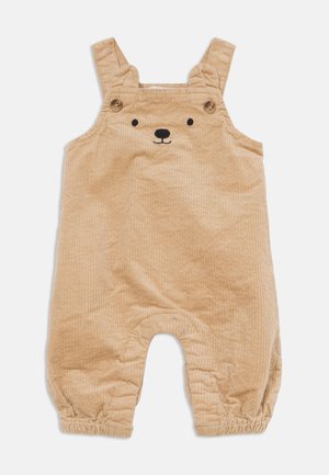 Combinaison bébé en velours côtelé beige avec bretelles, boutons en bois, chevilles élastiquées et un visage d’ours brodé sur la poitrine.