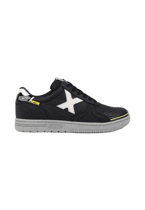 Zapatilla negra de corte bajo con logo blanco en forma de X, suela gris y lengüeta de talón con marca, mostrada de lado sobre un fondo blanco.