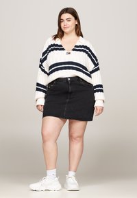 Un pull en tricot blanc avec des rayures marines et un col en V. Une jupe en denim noire avec des boutons sur le devant, portée avec des baskets blanches et des chaussettes blanches.