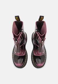 Botines de charol negro con acentos rosas, con cremalleras laterales, costuras amarillas y suela gruesa. Textura suave y acabado brillante.