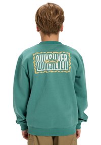 Türkise Sweatshirt aus weichem Stoff, mit einem großen grafischen Logo in Gelb und Weiß auf der Rückseite, sowie gerippten Bündchen und Saum.