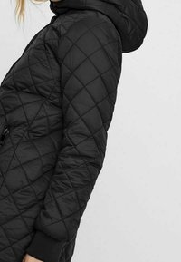 Veste matelassée noire avec une capuche, un motif de couture diagonal, des poches zippées et des poignets côtelés. Matériau synthétique léger.