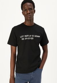 Svart bomull t-skjorte med hvit tekst "LOT REPLAY B. DENIM RD 39 423 925" over brystet. Korte ermer, rund hals, avslappet passform.