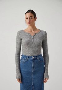 Gray ribbed long-sleeve top with a round neckline and button detail, paired with a high-waisted denim skirt in medium blue.