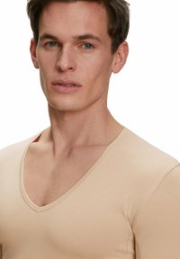 Beige, fitted V-neck shirt made of smooth fabric. Features short sleeves and a low neckline, emphasizing a minimalist design.