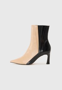 Bottines à bout pointu en cuir tan et noir, présentant une silhouette élégante, une forme effilée et un talon haut et fin.
