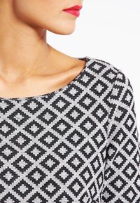 Maglione a righe in bianco e nero con un motivo a diamante. Collo rotondo e texture liscia con silhouette aderente.