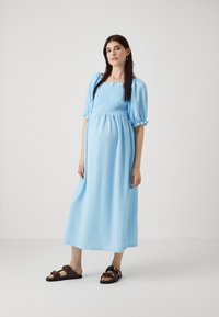 Rochie maxi texturată de culoare albastru deschis, cu decolteu pătrat și mâneci scurte puff. Asortată cu sandale maro, cu un design cu două curele.