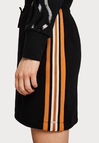Zwarte sweatshirt met oranje, crème en zwarte strepen aan de zijkant. Heeft een losse pasvorm en een zachte textuur. Inclusief logo-detail aan de zoom.