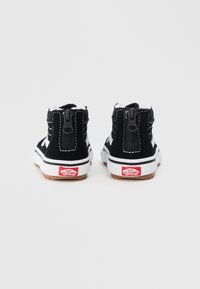 Par crnih i bijelih Vans visokih tenisica s patentnim zatvaračem na stražnjoj strani i "Vans Off The Wall" logotipima na bijelim gumiranim potplatima.