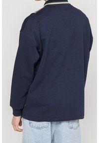 Persona vistiendo un sudadera azul marino con detalle de cuello a rayas y jeans de mezclilla azul claro, mostrada desde la espalda.