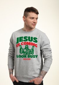 Šedá mikina s výrazným zeleným a červeným textem: "JESUS IS COMING LOOK BUSY" a grafikou postavy se zvednutýma rukama. Měkká tkanina, kulatý výstřih.
