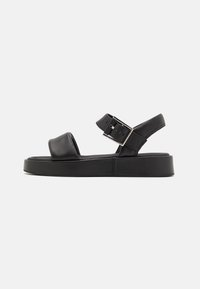 Sandalo in pelle nera con una vasta fascia anteriore, cinturino alla caviglia regolabile e una suola piattaforma spessa. Caratterizzato da una fibbia argentata e un design minimalista.