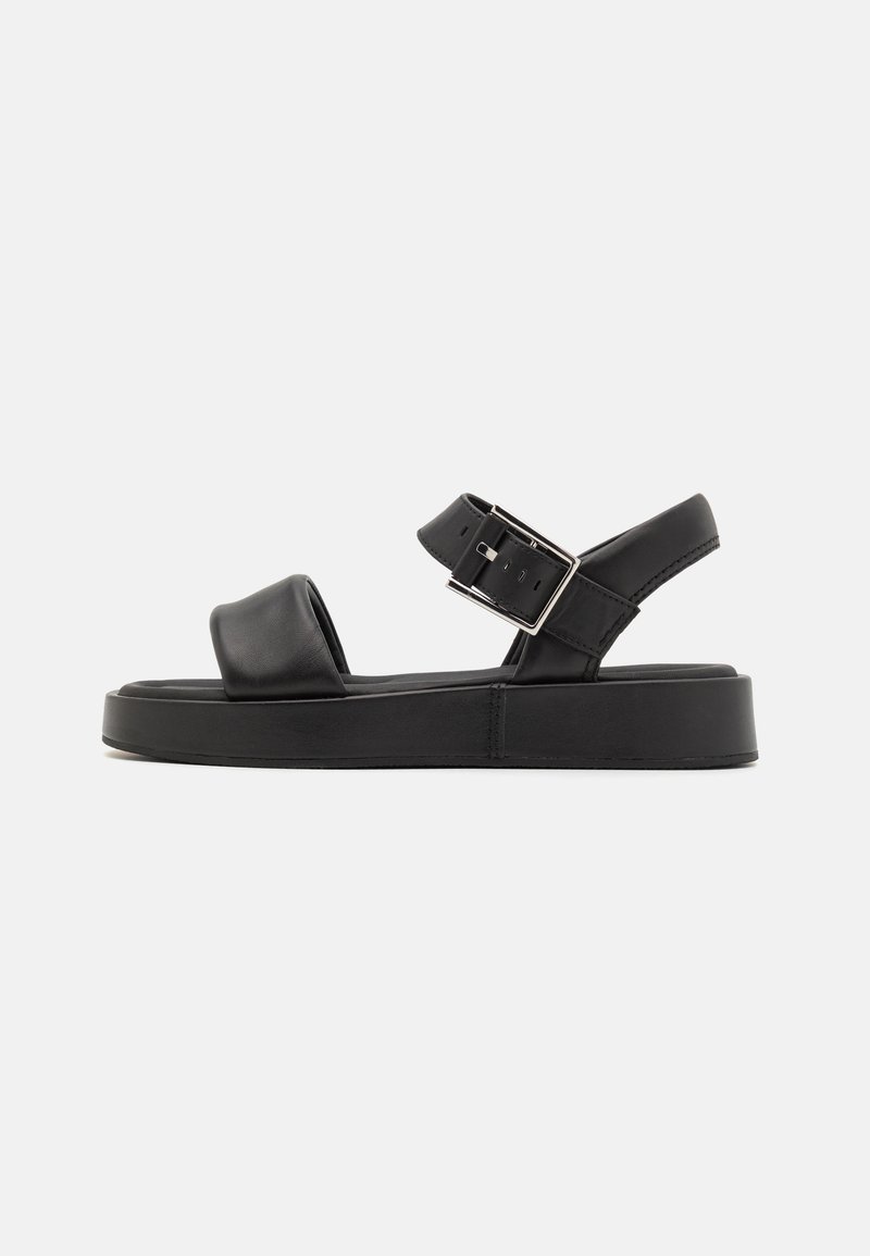 Sandalo in pelle nera con una vasta fascia anteriore, cinturino alla caviglia regolabile e una suola piattaforma spessa. Caratterizzato da una fibbia argentata e un design minimalista.