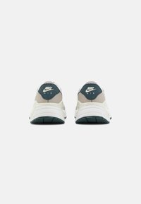 Sneaker Nike grigio e bianco con tomaia in tessuto texturizzato, caratterizzati da un accento verde scuro sul tallone e logo, e una suola bianca a contrasto.