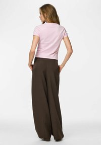 Rozā īsroku tops kopā ar plašām brūnām biksēm. Tops ir pieguļošs, bet biksēm ir augsta josta un plūstošs dizains.