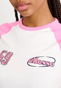 Camisa de manga raglán con un cuerpo blanco y mangas rosas. Muestra los logotipos bordados "59" y "ellesse" en colores contrastantes.