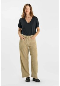 Zwarte V-hals t-shirt gecombineerd met brede beige broek met een gestructureerd patroon en strikceintuur. Model staat met de handen in de zakken.