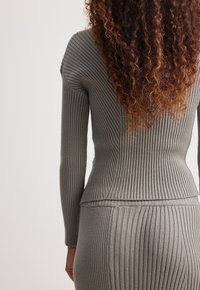 Haut en tricot côtelé gris à manches longues, présentant une silhouette ajustée et des lignes verticales. Texture douce avec un léger éclat.