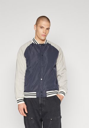 Navy and light gray bomber jacket with a button-front closure, ribbed cuffs, and striped neckline. Smooth fabric with raglan sleeves.
