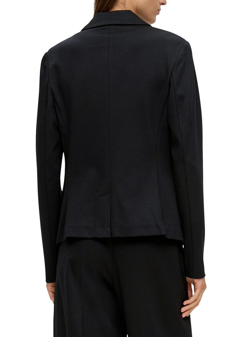 Blazer noir en tissu lisse, avec un col en pointe, des épaules structurées et un ourlet légèrement évasé avec une fente au dos.