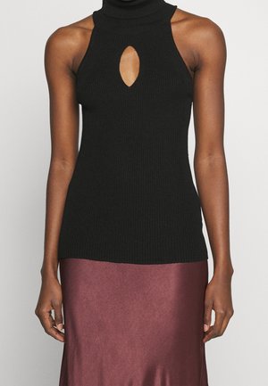 Femme portant un haut noir côtelé sans manches avec une ouverture en forme de trou de serrure et un col montant, associé à une jupe brillante mauve foncé.