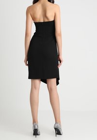 Černé šaty bez ramínek s přiléhavým korzetem a stylovým asymetrickým lemem. Hladký povrch tkaniny s výstřihem vzadu zakrytým zipem. Černo-bílé pruhované lodičky.