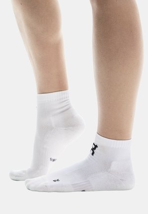 Chaussettes de sport blanches avec des bords côtelés, des semelles rembourrées et un logo de marque noir. Elles présentent une surface respirante et texturée ainsi qu'un talon renforcé.