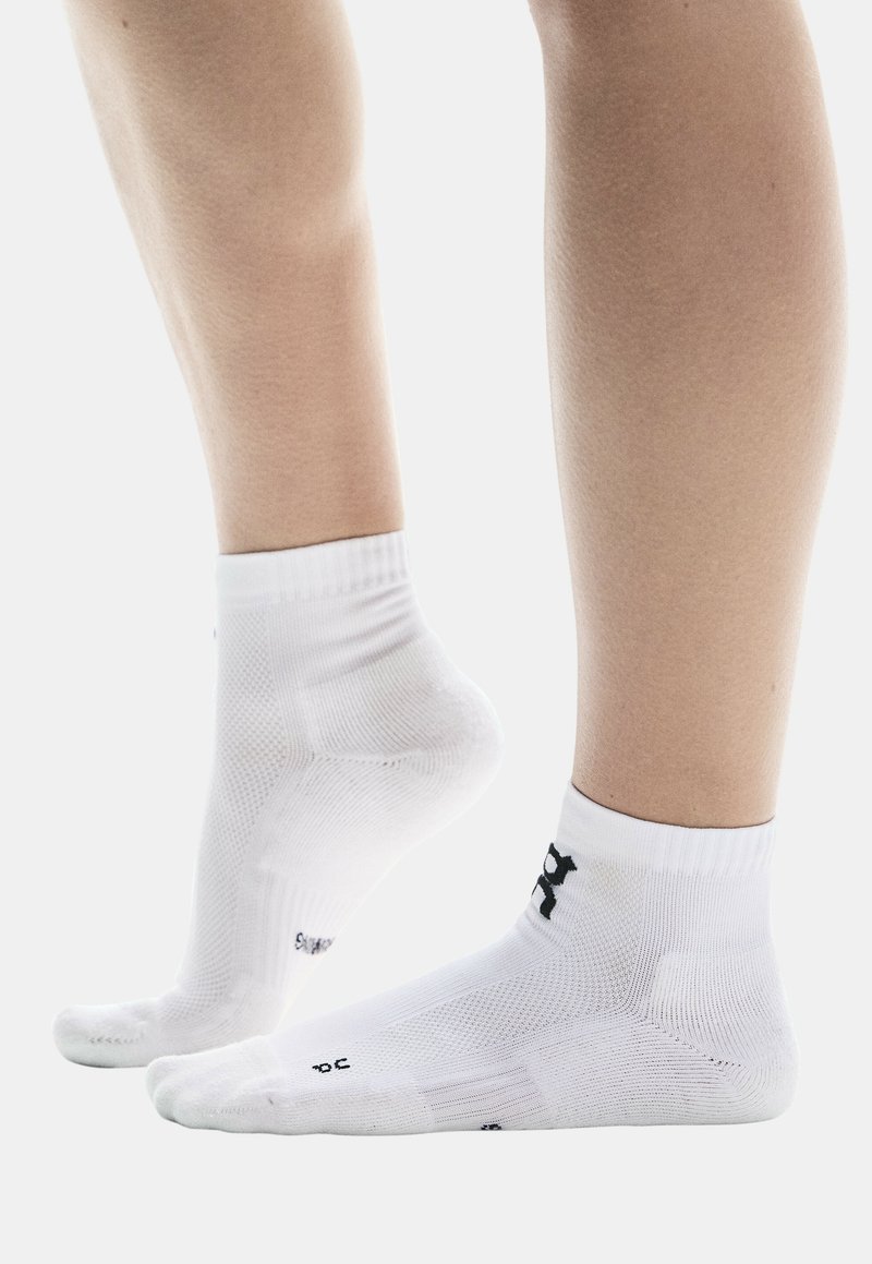 Weiße Sportsocken mit gerippten Bündchen, gepolsterten Sohlen und schwarzem Markenlogo. Verfügt über eine atmungsaktive, strukturierte Oberfläche und eine verstärkte Ferse.