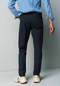 Marineblauwe chino's met een slim fit, voorzien van achterzakken en een gestructureerde stof. Gecombineerd met crèmekleurige sneakers met een cartoonaccent.