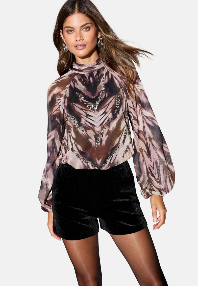 Kerge, pikakäistelise pluusiga, millel on roosa, pruuni ja musta abstraktne muster, kaunistatud sädelevate kivikestega; koos mustade sametist lühikeste pükstega.