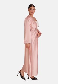 Lang, lyserød satinrobe med brede ærmer og en bundet talje, der har en glat tekstur og et flydende design, parret med sorte stilethæle.