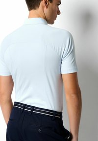 Hellblaues Polohemd mit tailliertem Schnitt, kurzen Ärmeln und klassischem Kragen; kombiniert mit dunkelblauen Hosen, die einen gestreiften Gürtel haben.