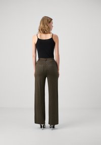 High-waisted olive green trousers with a wide-leg fit, featuring textured polka dots and a smooth waistband. Black tank top worn underneath.