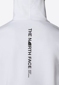 Vit huvtröja med en svart vertikal logotryck, "THE NORTH FACE" med "NEVER STOP EXPLORING" nedanför i fet stil. Mjuk textur.