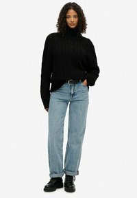 Czarny sweter z golfem w splot warkoczowy zestawiony z jasnoniebieskimi spodniami typu straight-leg. Uzupełniony czarnymi butami na sznurówki, z podwiniętymi mankietami.