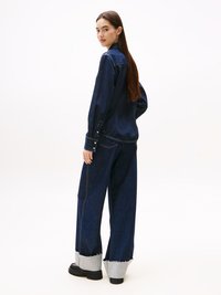 Dark blue denim outfit featuring a long-sleeve shirt and wide-leg pants with frayed gray cuffs, complemented by black footwear.