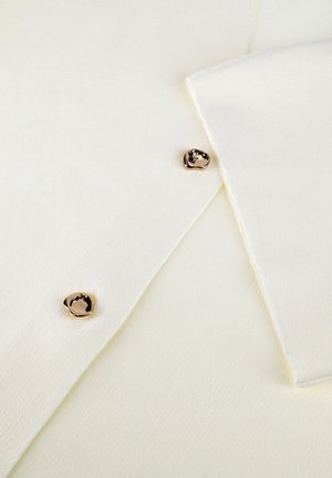 Close-up of white fabric with two irregular gold buttons and layered edges, highlighting texture and button details.