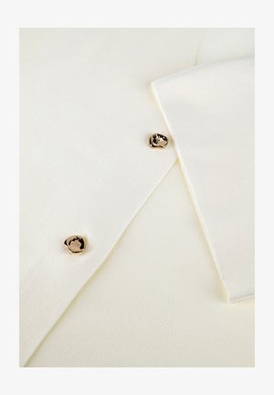 Close-up of white fabric with two irregular gold buttons and layered edges, highlighting texture and button details.