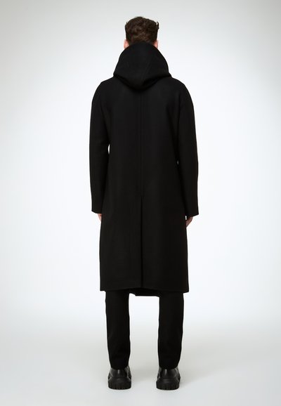 Schwarzer Wollmantel mit Kapuze, knieumspielend und mit geradem Schnitt, minimalistisch gestaltet und ohne sichtbare Beschläge. Matte Oberfläche.