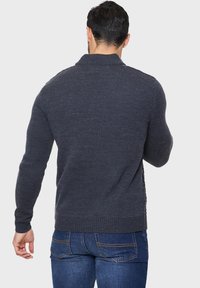Koolgrijze gebreide trui met een hoge kraag, ribbelstructuur en een getailleerd ontwerp. Heeft een schone achterkant en standaard mouwlengte.