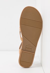 Tan vegan læder sandal med tynde stropper, en struktureret gummisål og mønstret slidbane. Har TOMS-mærkning på sålen.