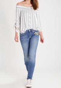 Off-shoulder vit topp med grå ränder, matchad med ljusblå jeans med slitna detaljer och fickprydnader. Vita sneakers.