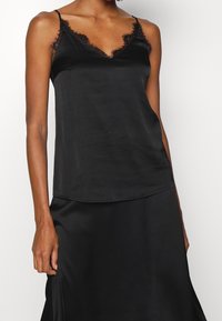 Svart satinkamisol med justerbara axelband, djup v-ringning och delikat spetskant längs kanterna. Har en len, glänsande textur.