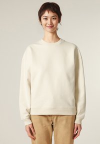 Felpa crema con collo a girocollo a coste e maniche lunghe. Texture liscia, vestibilità rilassata e colore uniforme senza motivi.