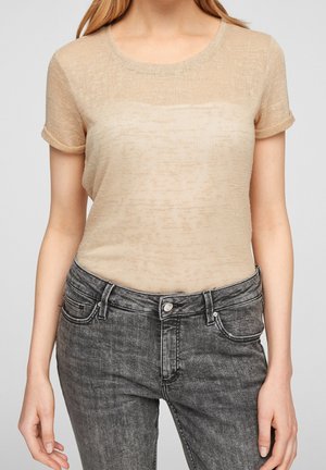 Top beige a maniche corte realizzato in tessuto leggero e strutturato con scollatura tonda, abbinato a jeans grigi con cuciture classiche e tasche.