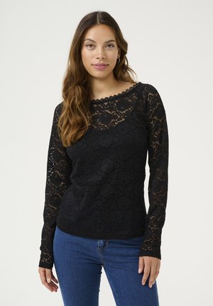 Zwarte kant langemouwtop met een geschulpte halslijn en bloemenpatroon; gedragen over blauwe denim jeans. Gestructureerde, semi-transparante stof.
