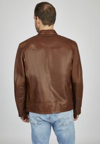 Chaqueta de cuero marrón con una textura suave, cuello alzado y cremalleras laterales, combinada con jeans de denim azul claro, vista desde la parte de atrás.