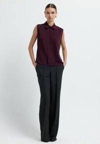 Blusa senza maniche bordeaux con colletto a bottoni e pieghe frontali, abbinata a pantaloni neri a righe sottili con vita alta.