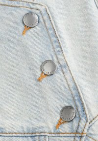 Jasnoniebieska tkanina dżinsowa z trzema srebrnymi metalowymi guzikami, widocznym pomarańczowym przeszyciem oraz lekka tekstura przypominająca klasyczny dżins.